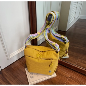 Detail of yellow nylon crossbody bag with purple patterned strap and double zippers