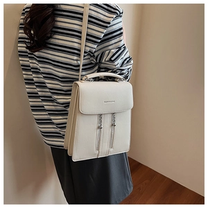 Detail of white square crossbody bag with decorative zippers and metal chain pendant