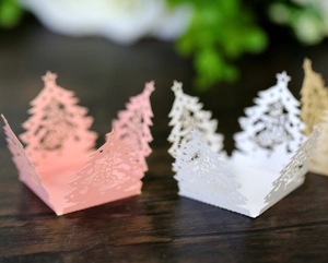 Laser-cut Christmas tree paper candy boxes in pink and white on a wooden surface