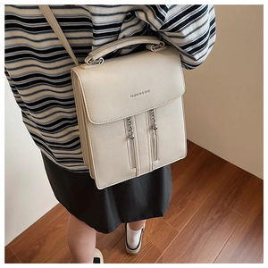 Detail shot of a beige leather handbag with dual decorative zippers and a silver pendant