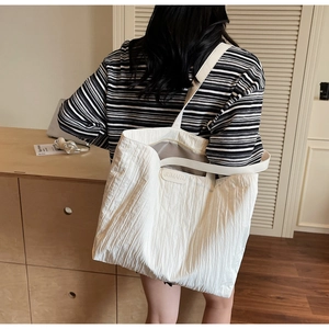 Detail shot of white tote bag with unique vertical pleated texture and leather logo tag