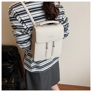 Rear view of model wearing a stylish beige leather backpack with decorative chain zippers
