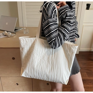Detail of white tote bag with pleated texture and grey logo label in casual office setting