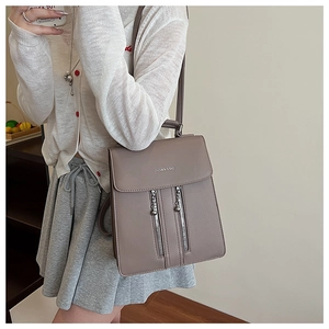 Détail d'un sac à dos en cuir taupe avec doubles fermetures éclair et pendentifs en métal