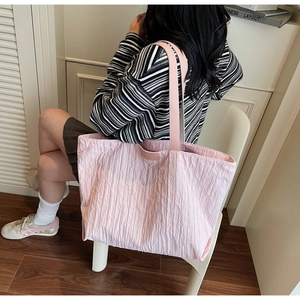 Detail of light pink tote bag featuring unique vertical pleated texture and branding plate