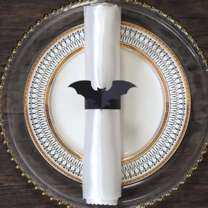 Close-up of a black bat napkin ring on white satin fabric for Halloween table setting
