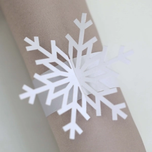 Close-up of a white laser-cut snowflake napkin ring on a beige cloth for Christmas decor