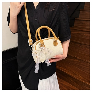 Detail of Boston bag with lychee texture, pearl charm, and lace bow on a wooden staircase