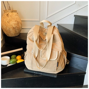 Detail view of water-resistant beige nylon backpack with multiple functional zip pockets