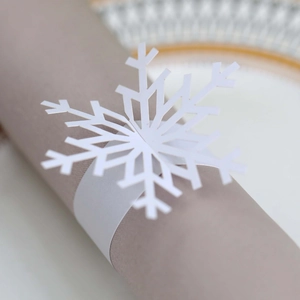 Close-up of white snowflake paper napkin ring with laser-cut hollow details on grey napkin