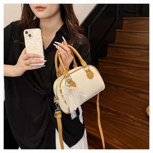 Close-up of cream Boston bag with lychee texture, yellow handles and pearl lace charm