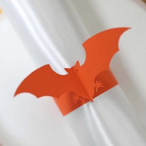 Close-up of orange paper bat napkin ring on a white silk napkin for Halloween table decor