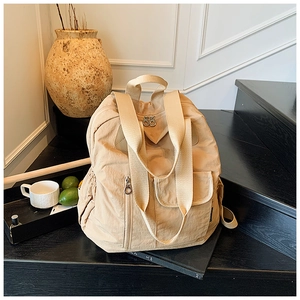 Detail view of a beige nylon backpack with double zipper closure on black steps