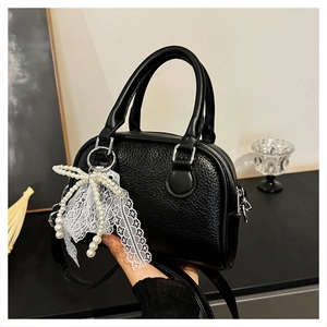 Close-up of black lychee grain leather Boston bag with white lace pearl charm