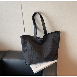 Detail of black tote bag featuring fine vertical pleated texture and JUMANJI leather patch