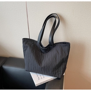 Detail of black pleated tote bag showing the vertical texture and brand tag with white book
