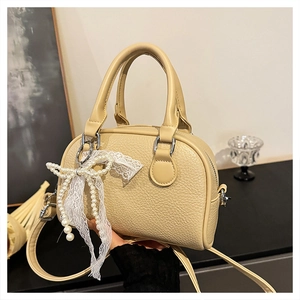 Close-up of beige lychee texture Boston bag with decorative pearl lace bow charm