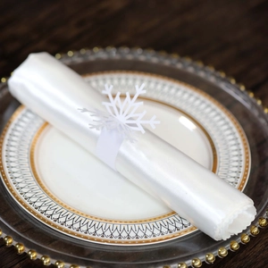 Close-up of elegant white snowflake napkin ring on satin fabric with festive dinnerware