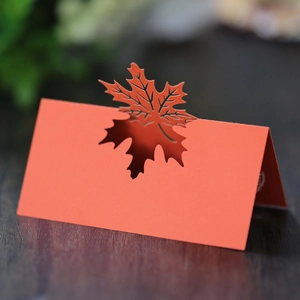 Close-up of laser-cut orange maple leaf place card on a rustic wooden table surface