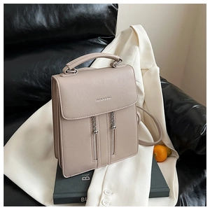 Detail view of the beige square backpack featuring dual vertical zippers and top handle