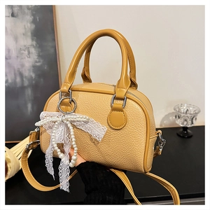 Detail of yellow lychee leather Boston bag with lace bow and pearl charm