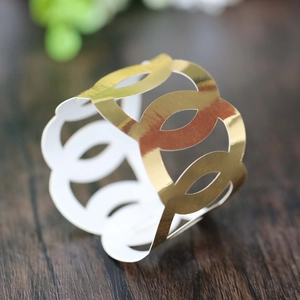 Detail of laser-cut gold interlocking oval napkin ring on dark wooden surface