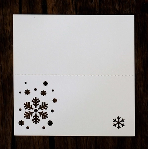 Detail of laser cut snowflake design on white place cards with wood grain background