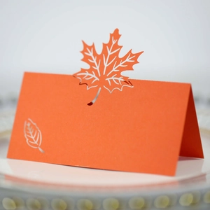 Macro detail of laser-cut orange maple leaf place card with hollow pattern for autumn events