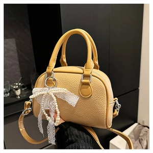 Detail of yellow lychee texture boston bag with pearl charm and lace bow accessory