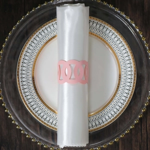 Detail of pink laser-cut paper napkin ring on white satin napkin and gold-edged plate