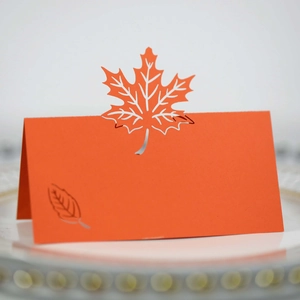 Detail view of a burnt orange hollow maple leaf place card on a white dinner plate