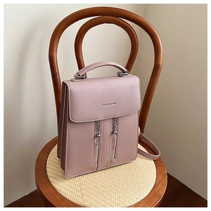 Detail of dusty pink square backpack with twin zippers and metal charms on leather texture