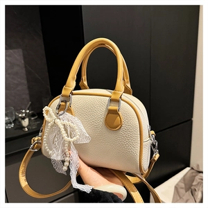 Detailed macro view of cream litchi texture PU leather bag with yellow handles and bow charm