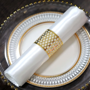 Close-up of golden hollow grid napkin ring on white satin napkin for luxury table setting