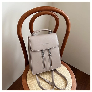 Detail of a beige leather backpack with decorative zippers and chain on a wooden chair