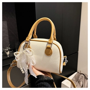 Detail of mini Boston bag in off-white lychee leather with yellow handles and bow charm