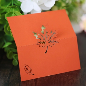 Laser-cut orange maple leaf place card featuring intricate hollow design for table settings