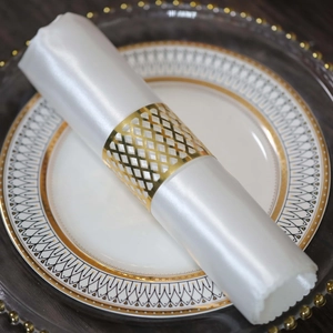 Macro shot of gold hollow grid napkin ring on white silk napkin over elegant plates