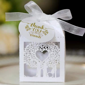 Detail of white laser-cut wedding favor box with hollow love tree pattern and white ribbon
