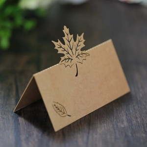 Close-up of a laser-cut maple leaf place card on a rustic dark wooden tabletop