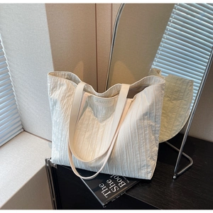 Detail of white pleated tote bag with large capacity and branded square logo patch