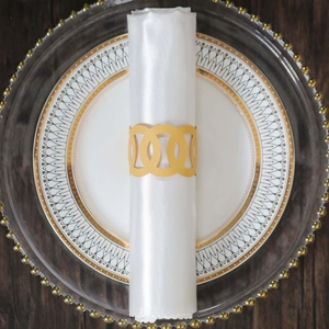 Close-up of golden hollow metal napkin ring on white satin napkin and black plate