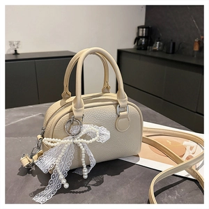 Detail of lychee textured cream crossbody bag with pearl lace bow and silver hardware