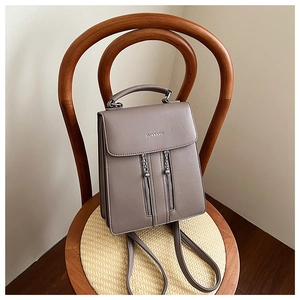Detail of taupe faux leather backpack with magnetic flap and metal zippers on a chair