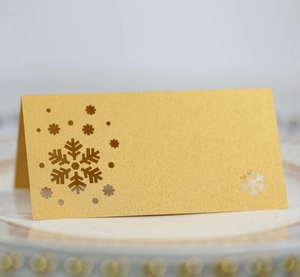 Detail of laser-cut snowflake place card in gold glitter paper on a white dining plate