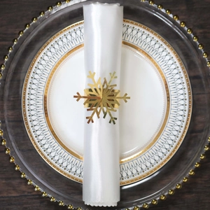 Close-up of golden snowflake napkin ring on white dinnerware over dark wood surface