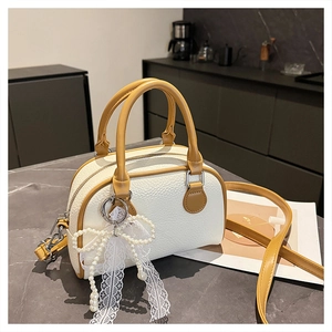 Detail of lychee textured leather boston bag with contrasting mustard yellow trim and pearl bow