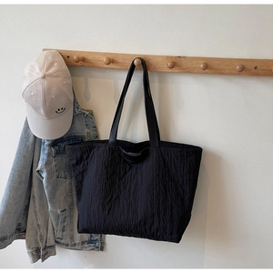 Minimalist black quilted tote bag displayed on a wooden rack with casual denim jacket