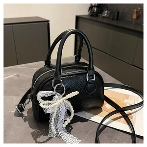 Detail of black lychee grain leather Boston bag with lace bow and pearl charm on marble