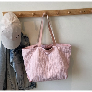 Detailed view of pink pleated tote bag texture and logo patch hanging on wooden hook